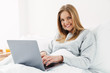 © Drobot Dean - Image of woman smiling and using laptop while lying in bad
