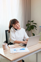 Asian Woman working on laptop at office while talking on phone