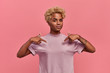 © antianti - Self assured proud African American woman has blonde hairstyle satisfied with her own high achievements, points with two hands at herself, or at a t-shirt for printing, isolated over pink background