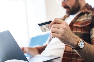 Canvas Print - Portrait of young man using laptop and credit card on sofa at home