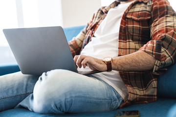 Sticker - Portrait of caucasian man using laptop while sitting on sofa at home