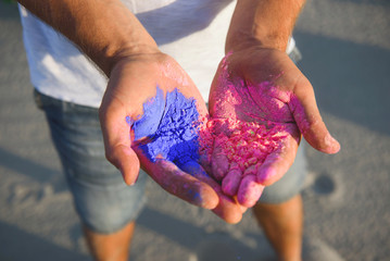 young guy in a white T-shirt and denim shorts holds multi-colored holi in his hands