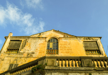 Canvas Print - Low angle view of the exterior of an old, abandoned house with scraped walls, damaged windows and a stone terrace and the roof against clear blue sky, Italy