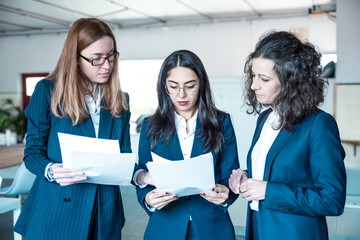 Wall Mural - Group of focused women reading paper documents. Front view of professional business team with instructions. Business concept