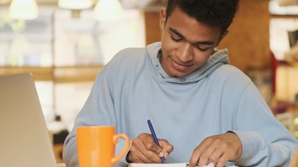 Canvas Print - Handsome smiling positive young african guy student studying doing homework.