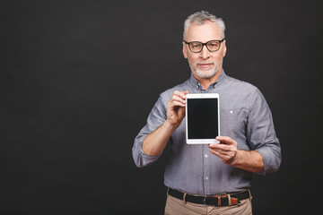 Wall Mural - Senior aged smiling man showing blank screen of tablet computer isolated against black background.