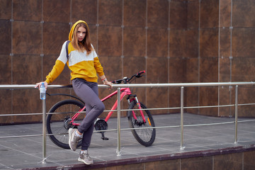 Wall Mural - A teenage girl near the marble wall sits on the railing with a red bicycle and a bottle of water