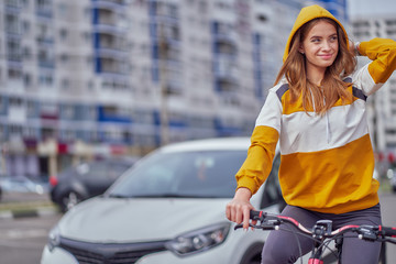 Wall Mural - The girl rides a bicycle around the city and straightens the hood with his hand.