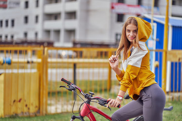 Wall Mural - Fashion girl model in a yellow jacket posing in the city, sitting on a bicycle.