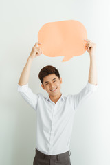 Wall Mural - Excited young Asian man holding empty speech bubble while standing over white background.