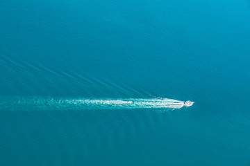 Wall Mural - Little speedboat following in the waves behind a big boat on a sunny day.