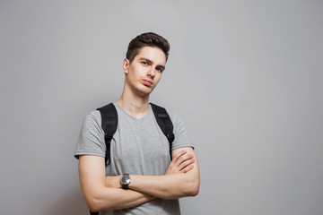 Young man in gray shirt on grey background. Student with backpack