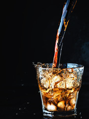 Cool, soft carbonated cola drink is poured into a glass of ice. Soda water refreshing drink isolated on dark background