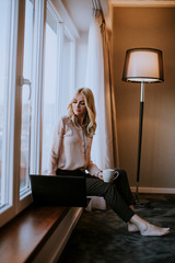 Young woman working on laptop  in living room on the window sill