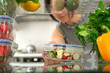 Woman looking inside a fridge full of food and choosing a salad in the container.