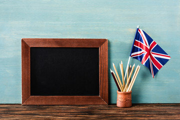 Wall Mural - empty chalkboard near pencils and uk flag on wooden table near blue wall