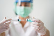 © pangoasis - Close up medical doctor wearing face shield, medical mask and medical grove. She holding draw syringe and bottle with Coronavirus vaccine for 2019-nCoV COVID virus.