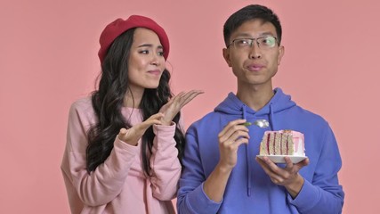 Poster - Young hungry woman looking how her boyfriend eat a cake isolated over pink wall background