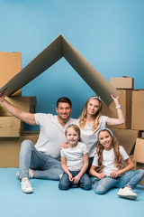 Wall Mural - positive parents holding carton roof over kids on blue with cardboard boxes for relocation