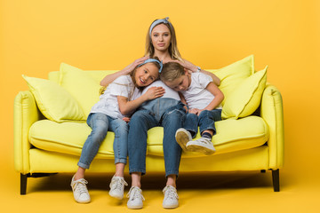 Wall Mural - pregnant mother hugging with smiling daughter and son on sofa on yellow