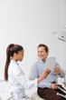 © LIGHTFIELD STUDIOS - happy patient looking at mirror near smiling african american dentist in braces