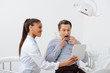 © LIGHTFIELD STUDIOS - terrified patient looking at mirror near cheerful african american dentist in braces