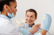 © LIGHTFIELD STUDIOS - selective focus of happy patient pointing with finger at teeth model near african american dentist in latex gloves