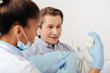 © LIGHTFIELD STUDIOS - selective focus of african american dentist in latex gloves pointing with finger at teeth model near patient