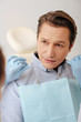 © LIGHTFIELD STUDIOS - selective focus of dentist in latex gloves holding dental floss near handsome patient