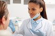 © LIGHTFIELD STUDIOS - selective focus of happy african american dentist in latex gloves pointing with hand at toothbrush near patient