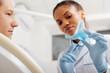 © LIGHTFIELD STUDIOS - selective focus of african american dentist in latex gloves pointing with finger at retainer near patient