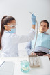 © LIGHTFIELD STUDIOS - african american dentist in medical mask and face shield holding stainless dental instrument near man