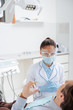 © LIGHTFIELD STUDIOS - selective focus of african american dentist in medical mask and face shield near man in clinic
