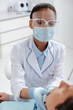 © LIGHTFIELD STUDIOS - selective focus of african american dentist in medical mask and face shield touching patient