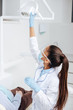 © LIGHTFIELD STUDIOS - african american dentist in medical mask and face shield touching medical lamp