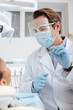 © LIGHTFIELD STUDIOS - selective focus of dentist in medical mask, face shield and latex gloves holding dental instrument near african american woman