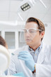 © LIGHTFIELD STUDIOS - selective focus of dentist in protective face shield holding dental mirror near african american woman