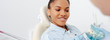 © LIGHTFIELD STUDIOS - panoramic shot of happy african american woman in braces near dentist holding teeth model