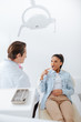 © LIGHTFIELD STUDIOS - selective focus of african american woman pointing with finger at opened mouth while looking at dentist in clinic