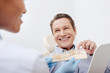 © LIGHTFIELD STUDIOS - selective focus of happy patient pointing with finger at teeth palette near cheerful african american dentist