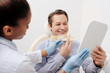 © LIGHTFIELD STUDIOS - selective focus of african american dentist holding teeth palette near cheerful patient looking at mirror