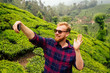 bloger redhaired ginger male enjoying morning taking selfie pictures on camera of smartphone in India chai plantations Munnar