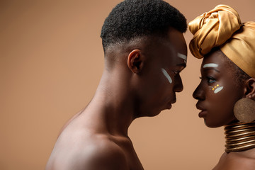 side view of naked tribal afro couple posing face to face on beige