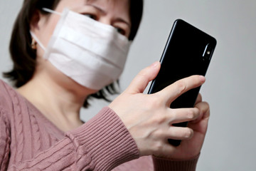 Coronavirus protection, woman in medical mask using smartphone, close-up mobile phone in female hands. Concept of fever, search for covid-19 symptoms