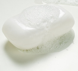 A wet bar of regular white soap bar with bubbles and water.