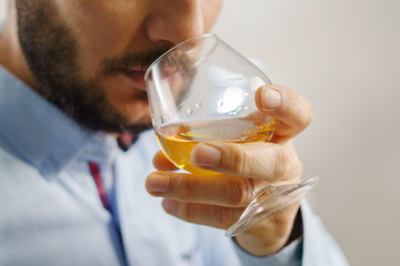 Hand of adult caucasian man wearing shirt holding glass of cognac brandy tasting at home at evening or night close up male with beard and short hair at home alone one