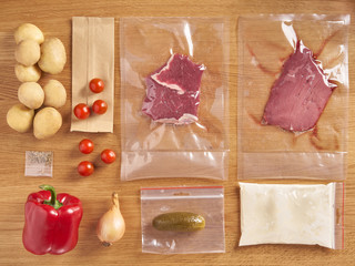 delivery set of packaged food for dinner. meat in plactic bag and vegetables: potatoes, onions, spic