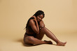 © Indico Studio/ADDICTIVE STOCK - Curvy beautiful African American woman with braids in lingerie looking at camera sitting on the floor against yellow background