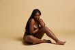 © Indico Studio/ADDICTIVE STOCK - Curvy beautiful African American woman with braids in lingerie looking down sitting on the floor against yellow background