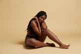 Curvy beautiful African American woman with braids in lingerie looking at  camera sitting on the floor against yellow background Stock Photo